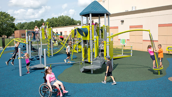 Children playing on a playground with a girl in a wheelchair in the foreground.