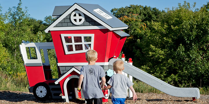 Two little boys from behind walking to a fire station play house. 