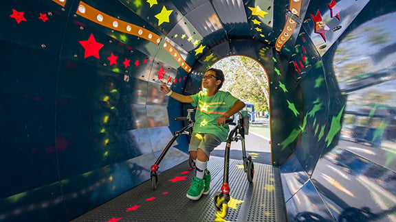 Child on a mobility structure touching the walls of a sensory tunnel.