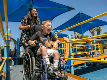 Boy in wheelchair smiling on adaptive playground equipment ramp