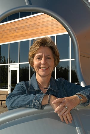 Barb King co founder of Landscape Structures posing for a photo while leaning on a Mobius Climber.