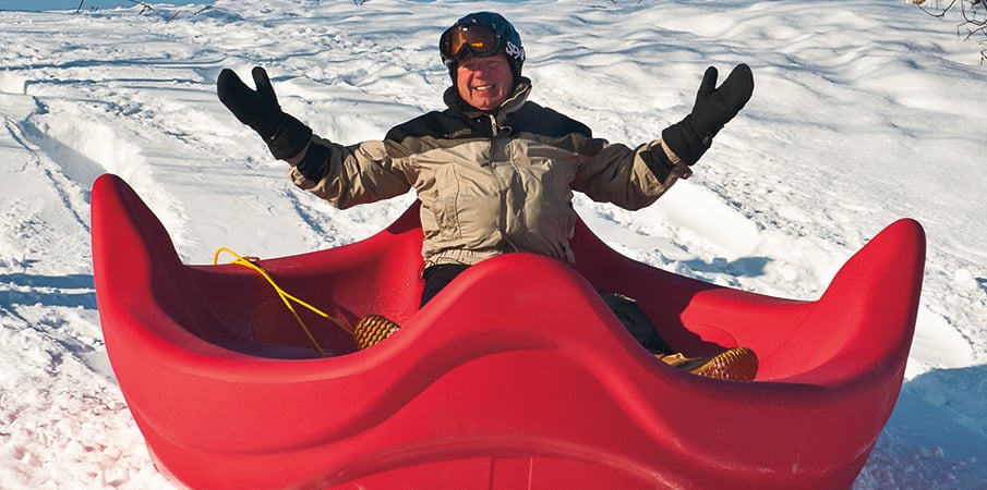 Steve King Landscape Structure founder sliding down a hill using a OmniSpin as a large sled.