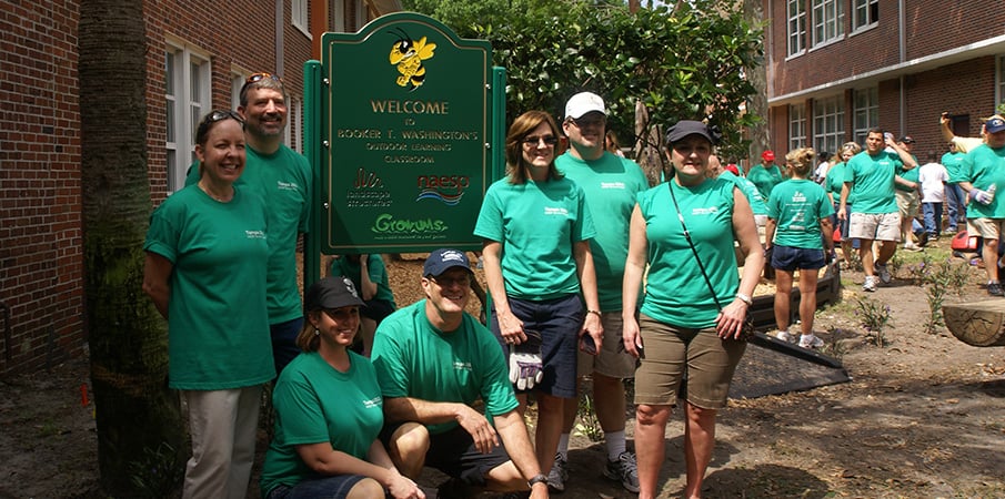 Volunteer playground builders stand next to a welcome sign to a new park.