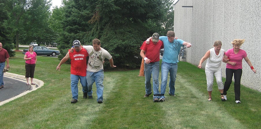 Landscape Structure employees race in a three legged race outside.

