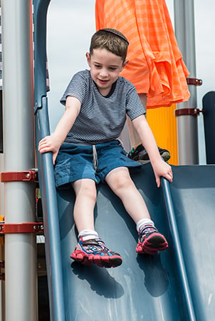 Young boy sliding down a PlayBooster Double Swoosh Slide.