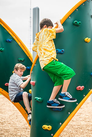 Kids climbing on a PlayBooster curved playground climber with foot and hand holds.