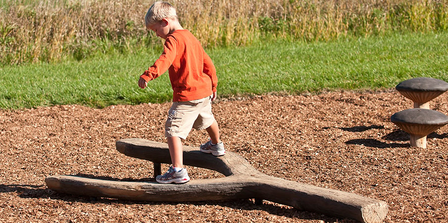 Young boy walking on log balance beam.
