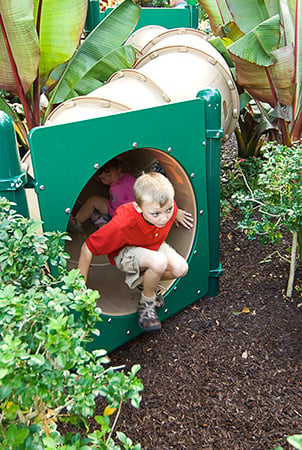 A young boy climbs out of the exit of a ground S crawl tunnel.