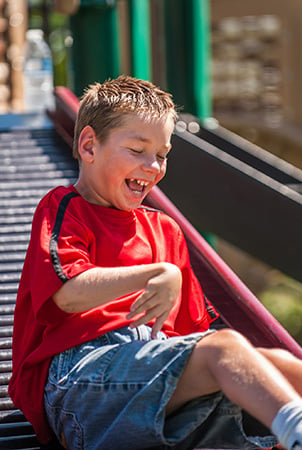 A little boy laughs as he has just finished sliding down the rollerslide. 