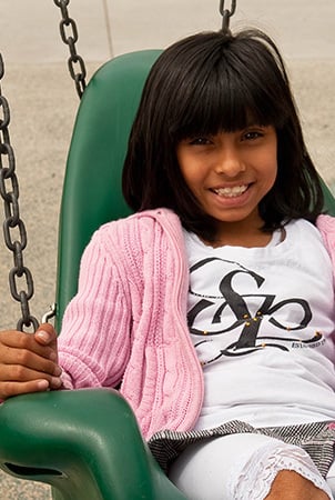 A girl smiles as she sits in a green adaptive swing. 