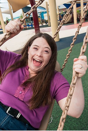 A young woman laughs as she swings sideways on an adaptive swing. 