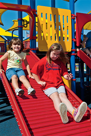 Two girls slide down a red rollerslide. 