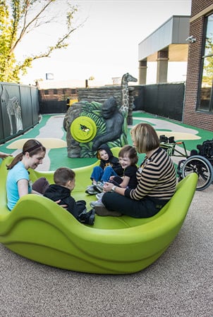 Children and adults sit in a lime green freestanding playground component. 