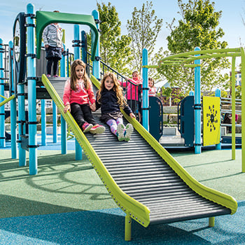 Two girls slide down a Rollerslide, which is an inclusive sensory alternative to traditional playground slides