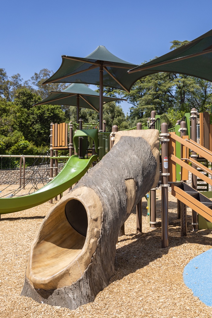 A custom GFRC (glass-fiber-reinforced concrete) playground equipment slide that is designed to appear like a hollow log