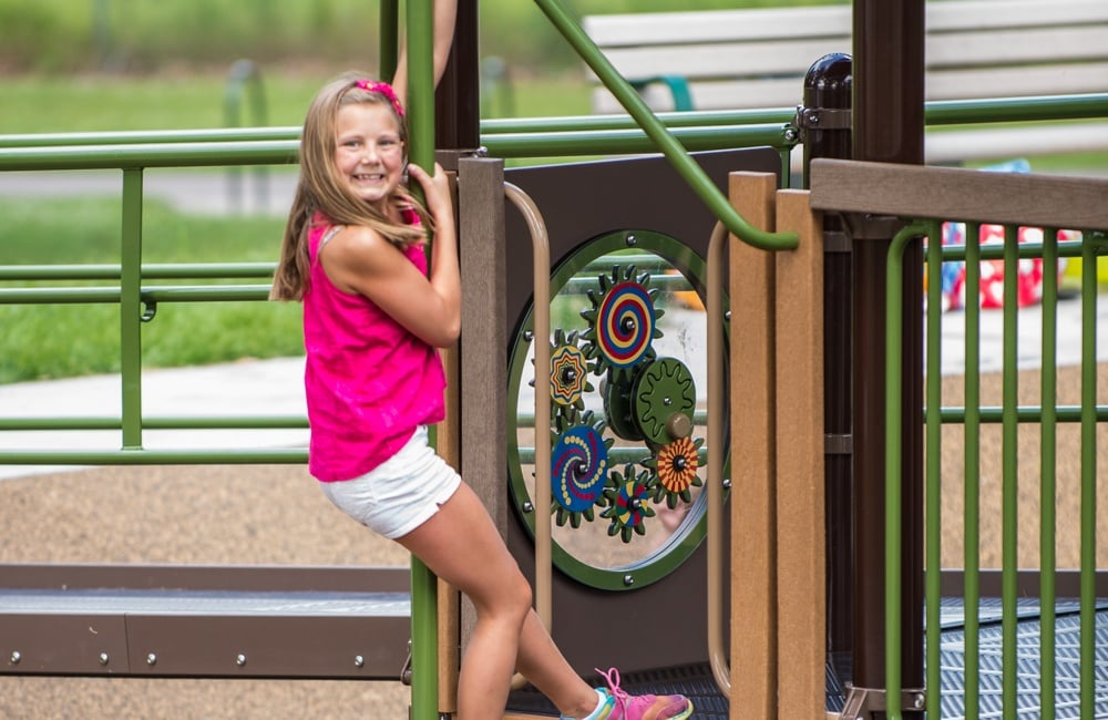 Girl grips a commercial playground slide, or firepole, that is a component of a larger playground structure
