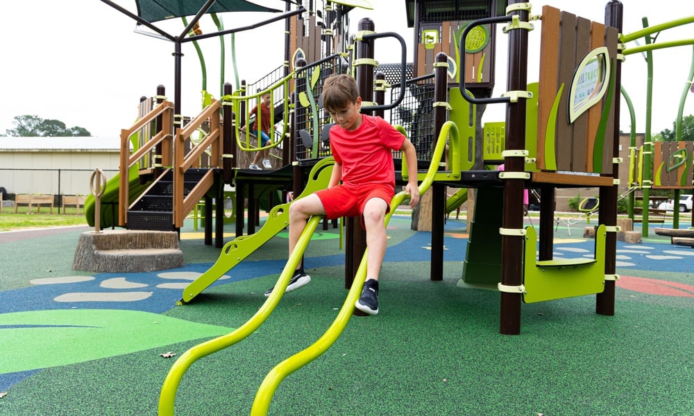 Boy slides down a commercial playground glider, which is a type of slide for playgrounds, that uses two steel rods instead of a typical slide bed