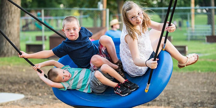A girl and two boys swinging on an Oodle swing. 