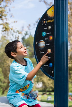 A boy pointing at a sign that has images and names of the solar system. 