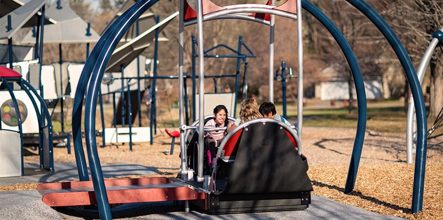 Three children playing in We-Go-Swing, one girl is in wheelchair.