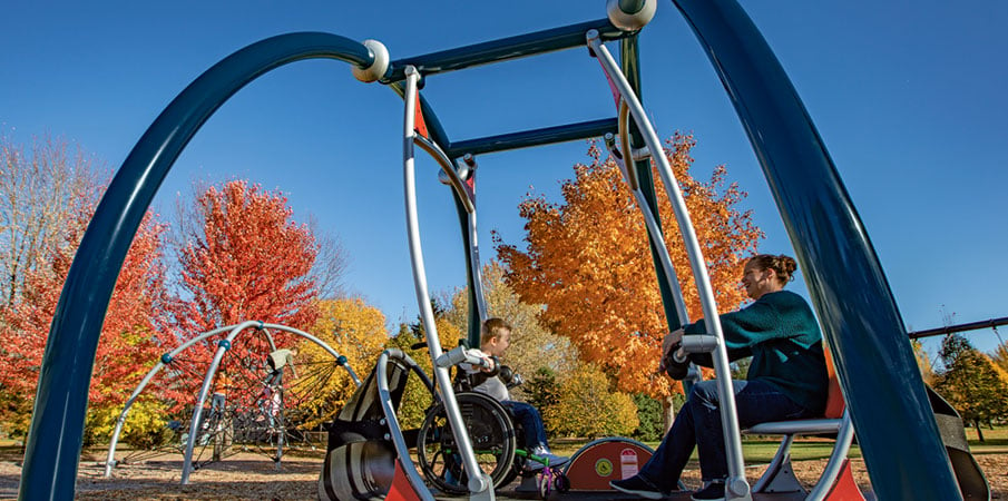 An adult and child swinging in We-Go-Swing, the child is in a wheelchair.