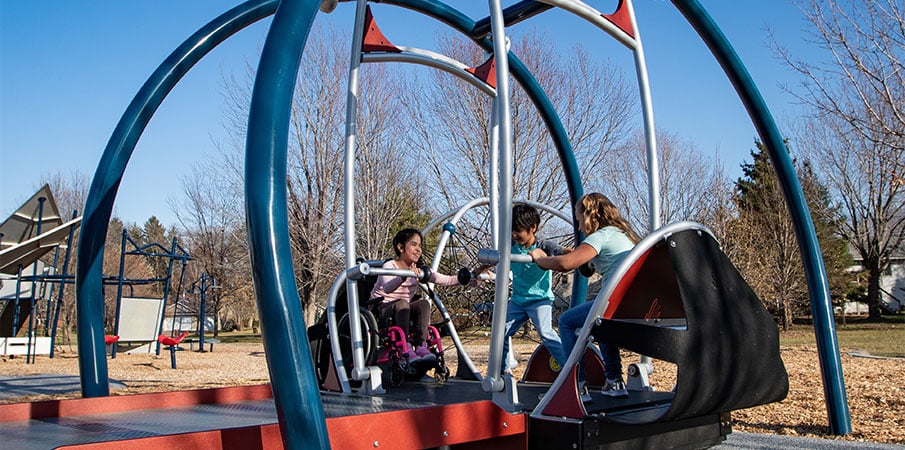 Three  children playing in a We-Go-Swing, one girl is in a wheelchair.