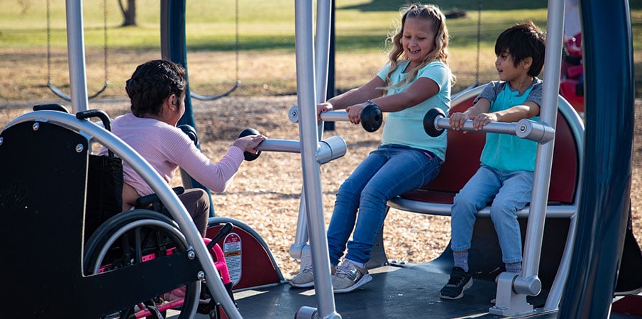 Three children playing on We-Go-Swing with one little girl in a wheelchair.