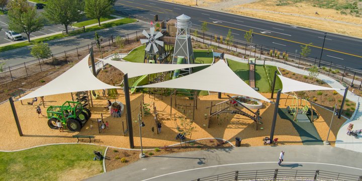 Farm and countryside themed playground with a custom silo play structure and windmill play structure in the background and a green custom tractor climber in the foreground. 
