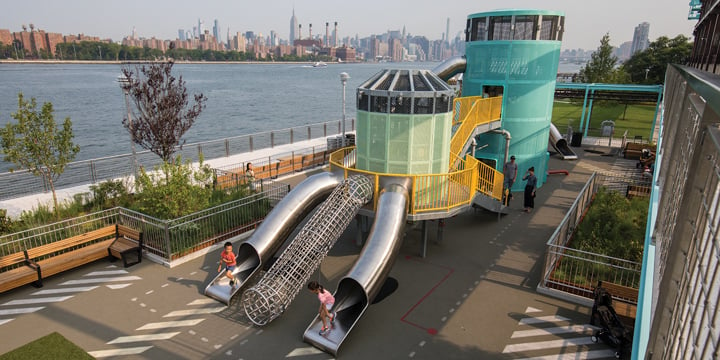 Bird's eye view of Domino Park playground with river in the background and New York City skyline in the distance. 