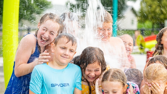 Children at a splash pad getting water poured on their heads from an overhead bucket above