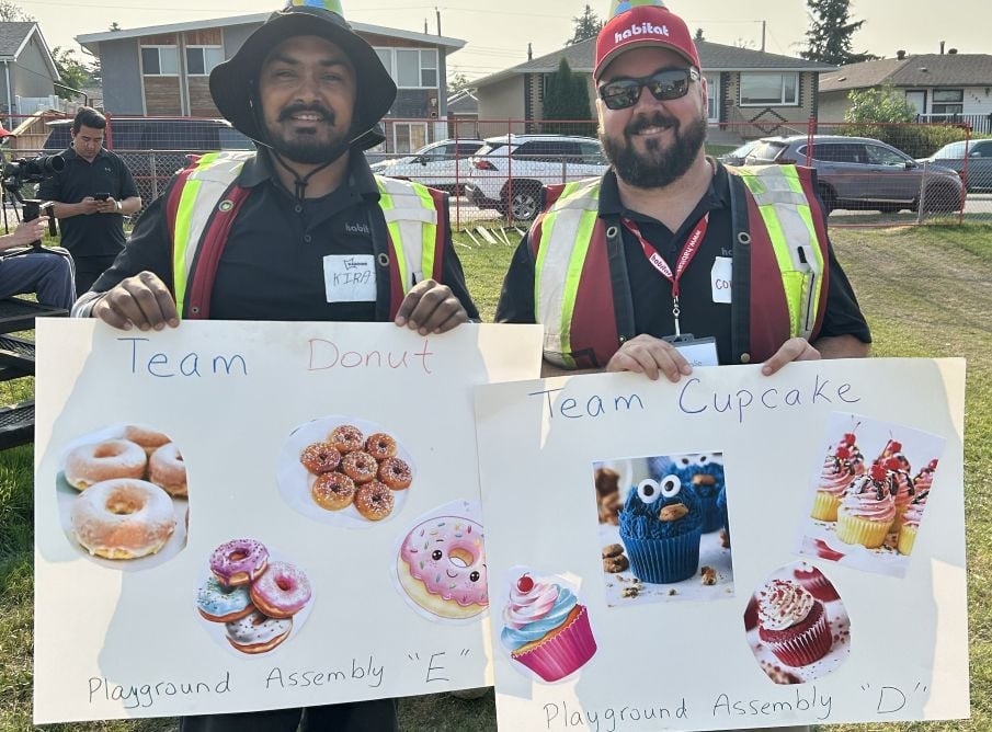 Two men stand side-by-side, each holding a homemade sign. One says "Team Donut" and the other "Team Cupcake"
