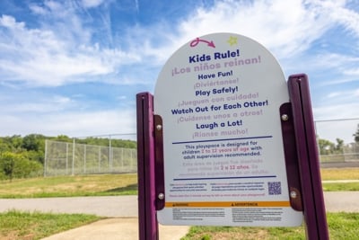 A playground sign reading "Kids Rule!" at the top with multiple other statements in English and Spanish