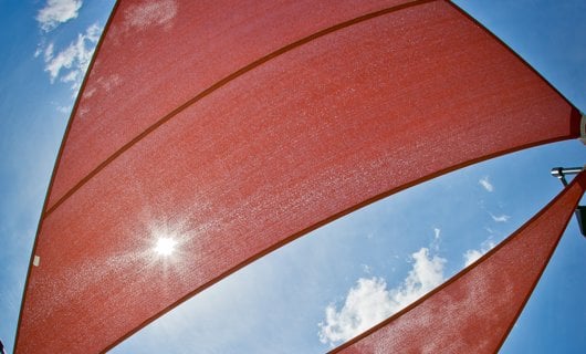 Looking up at a red shade sail with the sun filtering through