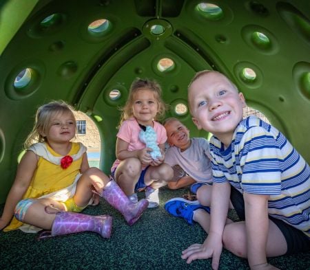 Four children smile at the camera from inside a Cozy Dome playground structure