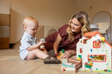 A woman lies on her side watching a toddler hold and look intently at an object