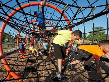 Kids climbing up down, over and through a playground net climber.