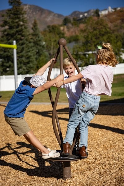 Three children ride on a playground spinner