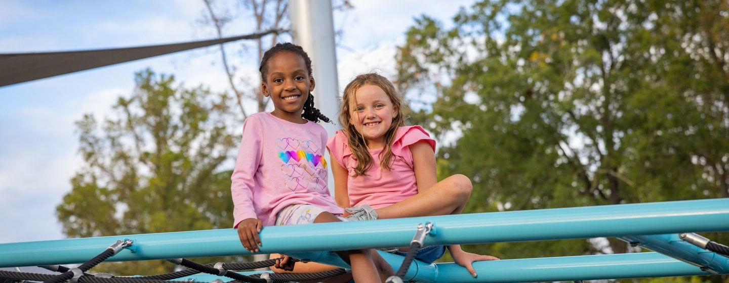 Two girls sit atop a net climber on a playground