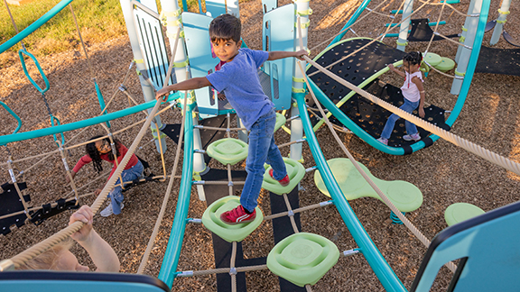 A child walking up a playground climber made of lime green stepping pods and cable net