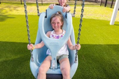 Girl smiles at camera from a swing with upper body support