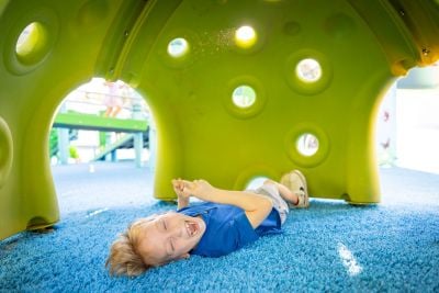 A boy laughs while lying on his back under a Cozy Dome play structure