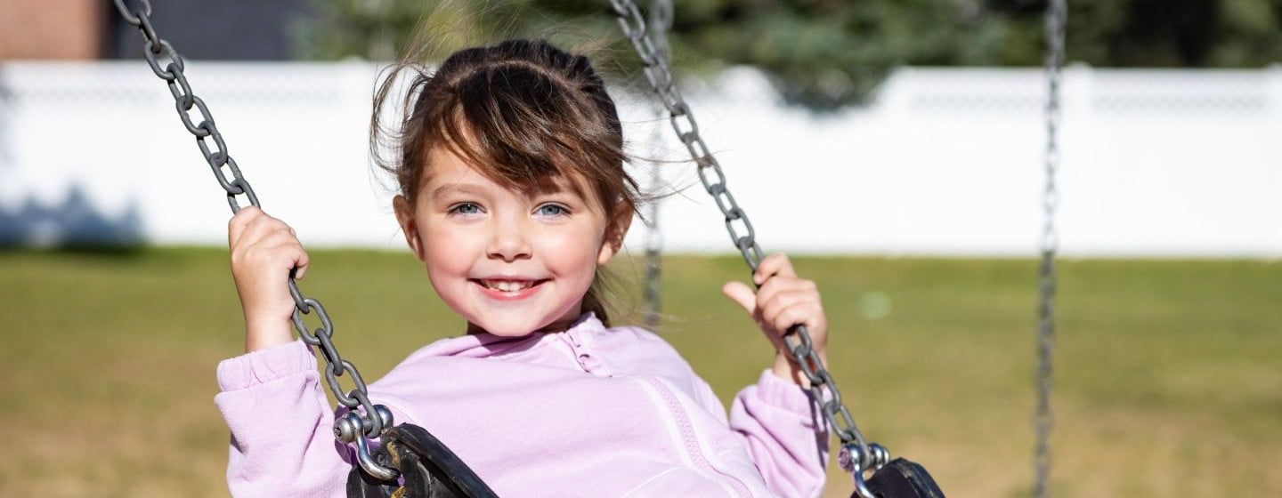 Close up of a young girl on a swing, smiling at the camera