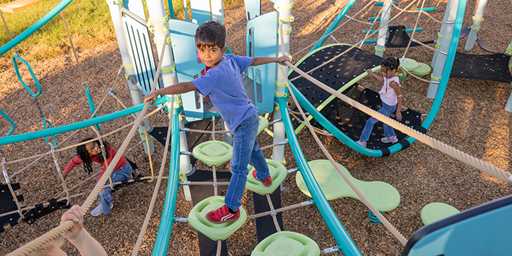 A child looking back at the camera as they navigate across a cable bridge with green steps 