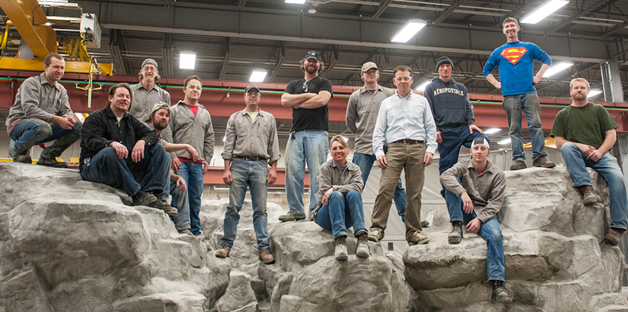 The concrete group at Landscape Structures stand and sit on two rock climbers inside a manufacturing building.