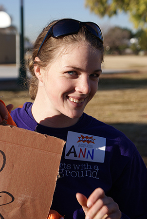 A woman smiles into the camera. She has a nametag that reads "Kaboom!" and "Ann" 