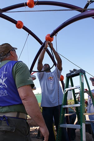 A man installs an overhead part of a playground structure. 