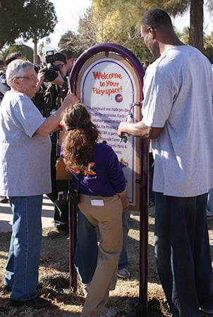 Three adults install a sign that reads "Welcome to your Playspace!" 