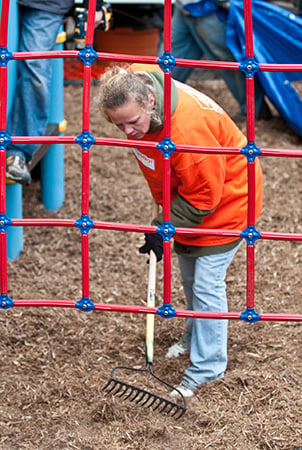 A woman rakes mulch at a playground installation site. 
