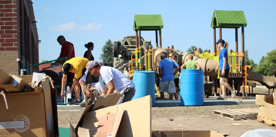View across piles of cardboard boxes of volunteers building a playground.