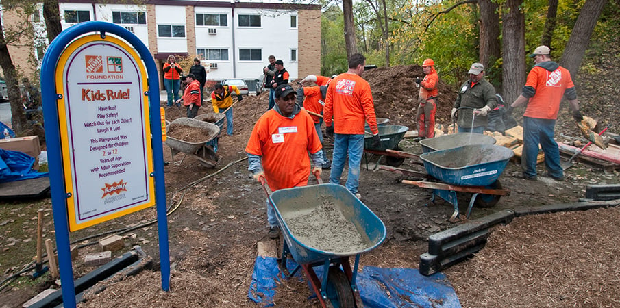 KABOOM! volunteer pushing wheelbarrow with concrete at a playground building site.